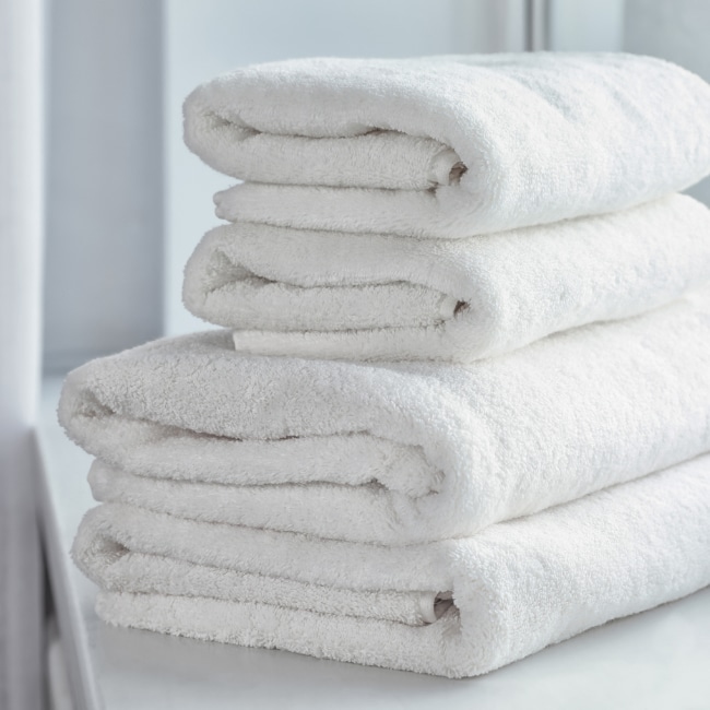 A stack of four neatly folded white towels provided by Able, placed on a white surface.