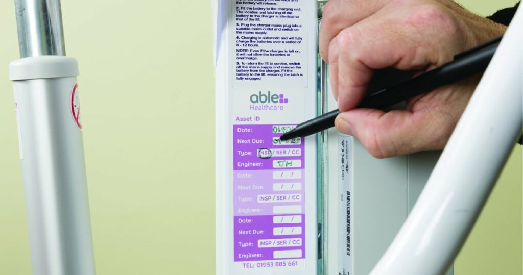 Person marking a maintenance checklist label for healthcare equipment with a pen.