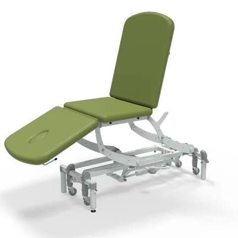 Adjustable medical examination table with green upholstery and a white metal frame, featuring segmented sections for back and leg support.