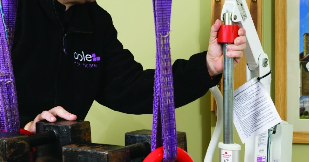 A person operates a patient lift with a purple support strap and control lever. A printed instruction sheet is visible.