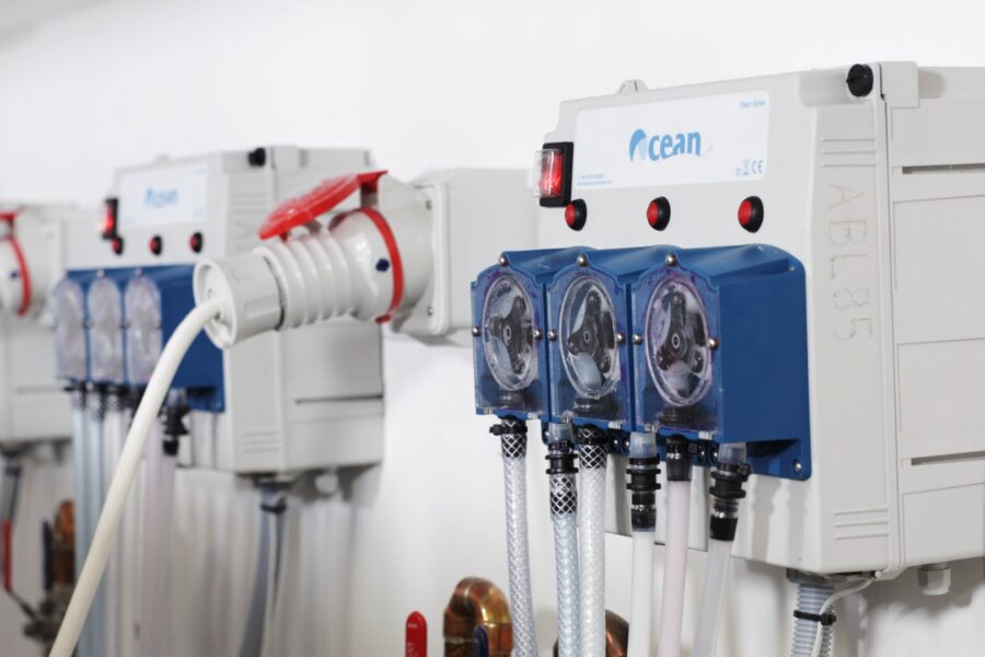 An auto dose system on the wall. A great Eco-Friendly Laundry Solutions for Care Homes. It's blue and grey with dials for dispensing laundry chemicals.