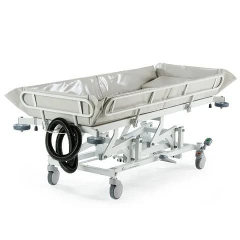 A medical stretcher with a padded surface, adjustable frame, and wheels is shown on a white background. A coiled hose is attached to the side.