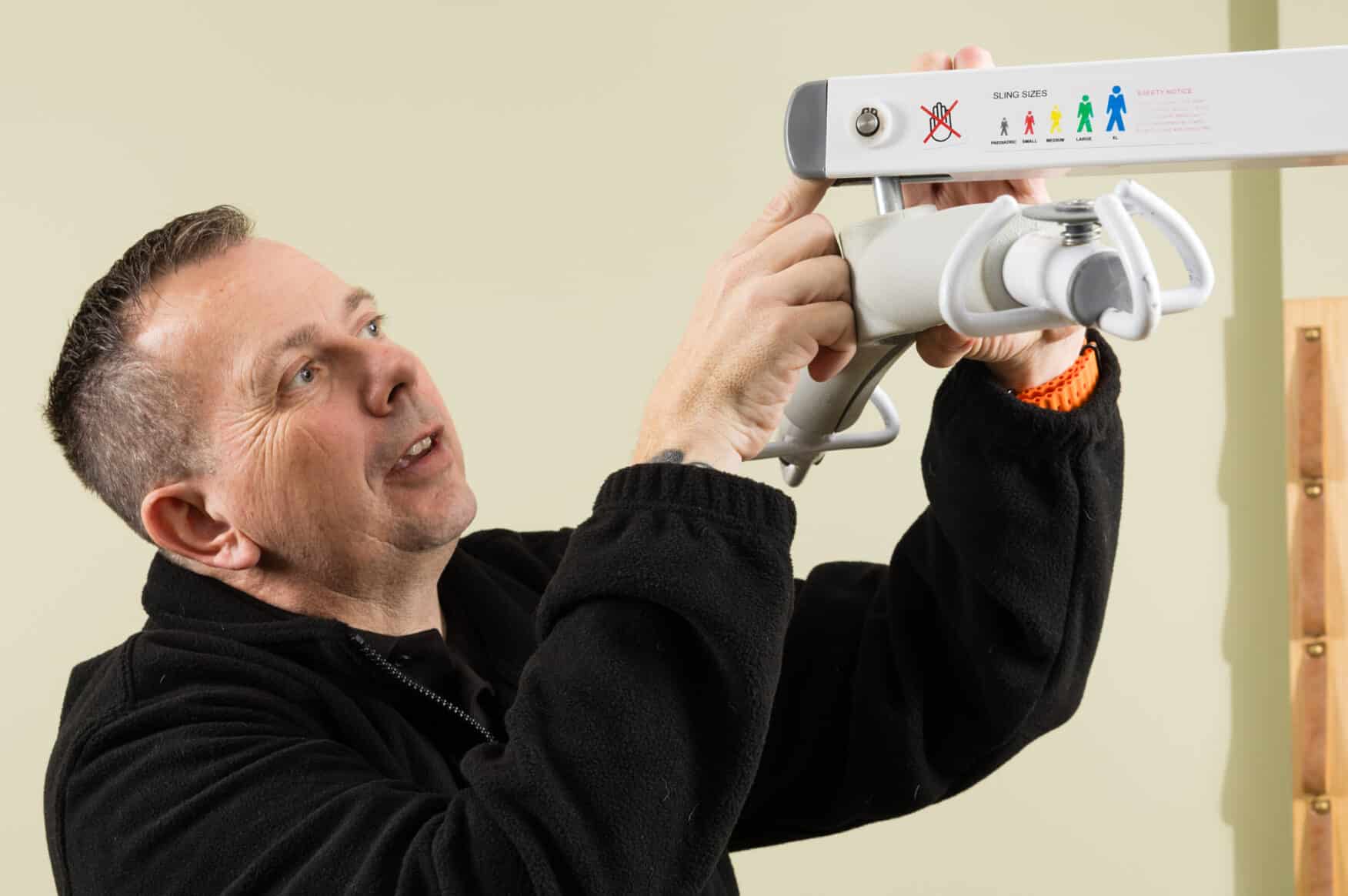 A man in a black jacket adjusts a sling hoist mechanism mounted on a wall for a LOLER test in Norfolk.