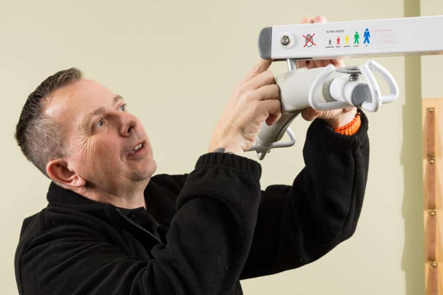 A man in a black jacket adjusts a sling hoist mechanism mounted on a wall for a LOLER test in Norfolk.