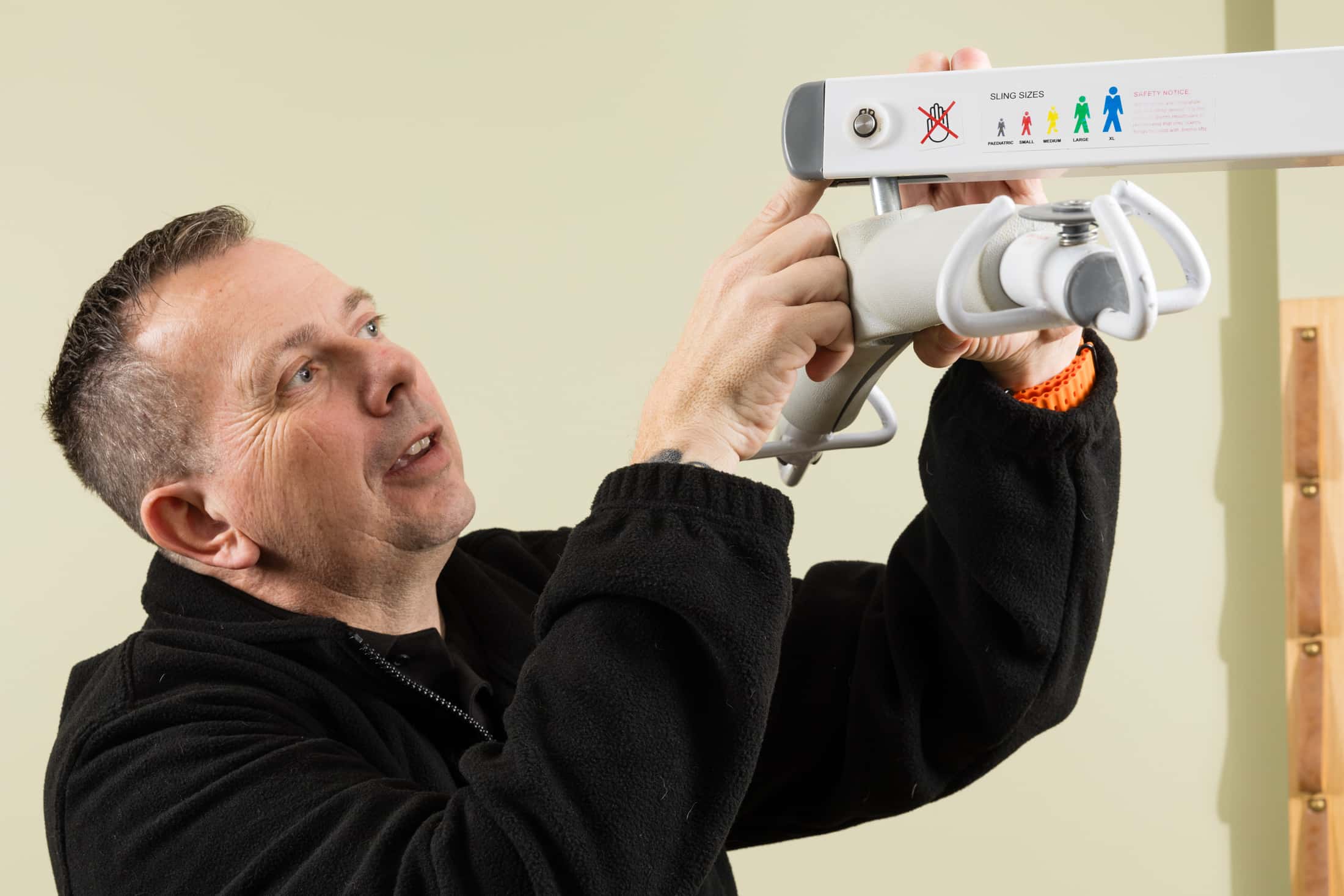 A man in a black jacket adjusts a sling hoist mechanism mounted on a wall for a LOLER test in Norfolk.