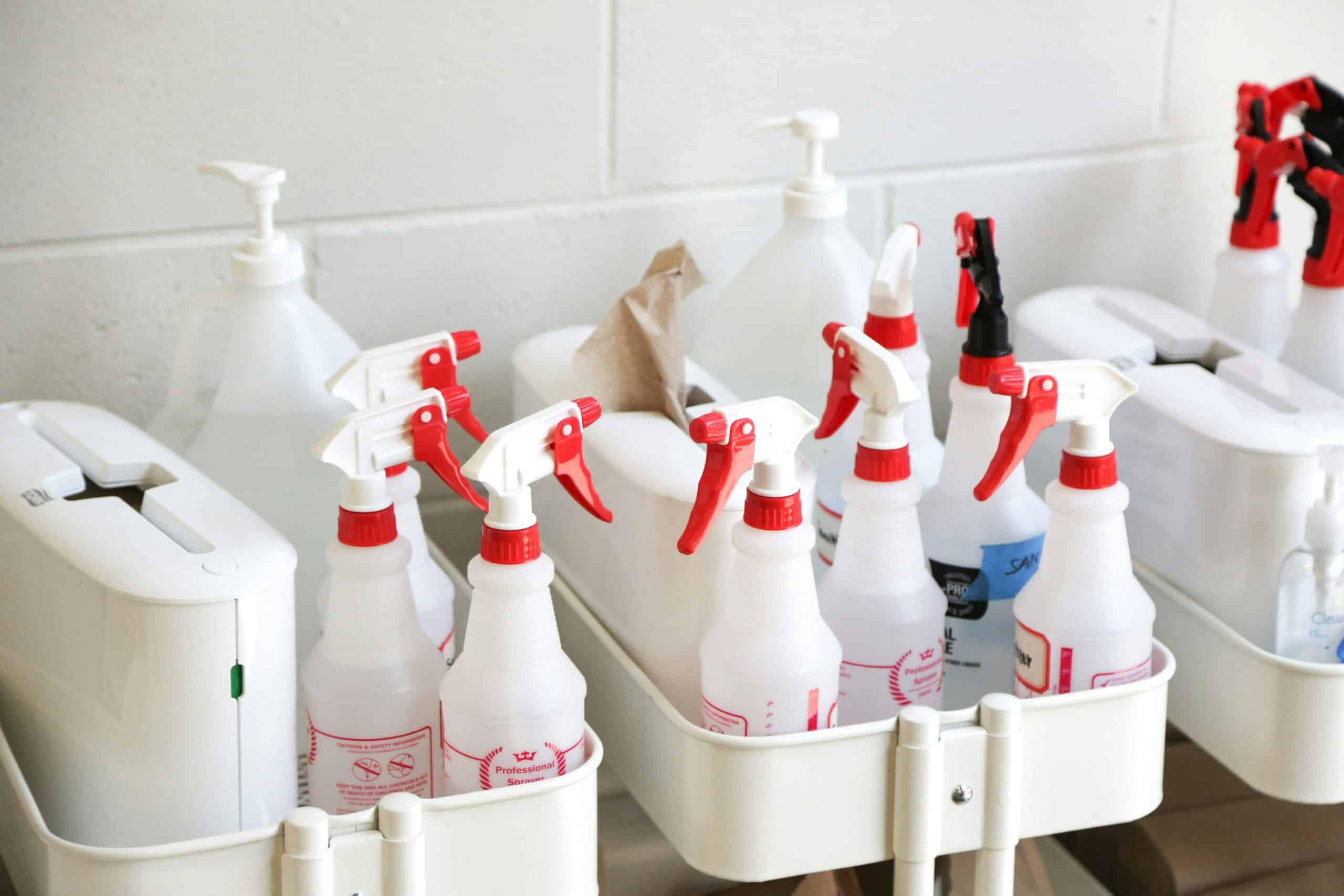 Multiple red-and-white disinfectant spray bottles and cleaning supplies on a cart in a care home setting.