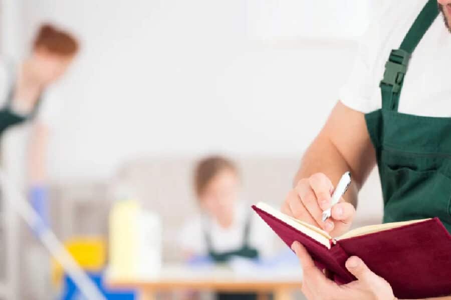 Care home cleaner writing in an audit checklist while team cleans in the background