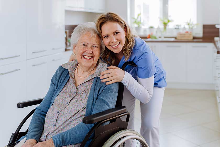 Smiling care home resident in a wheelchair with a nurse beside her in a modern care setting