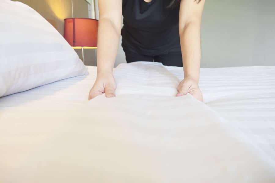 A carer making a neatly dressed bed with crisp white care home linen, showing comfort and quality in a resident’s room.