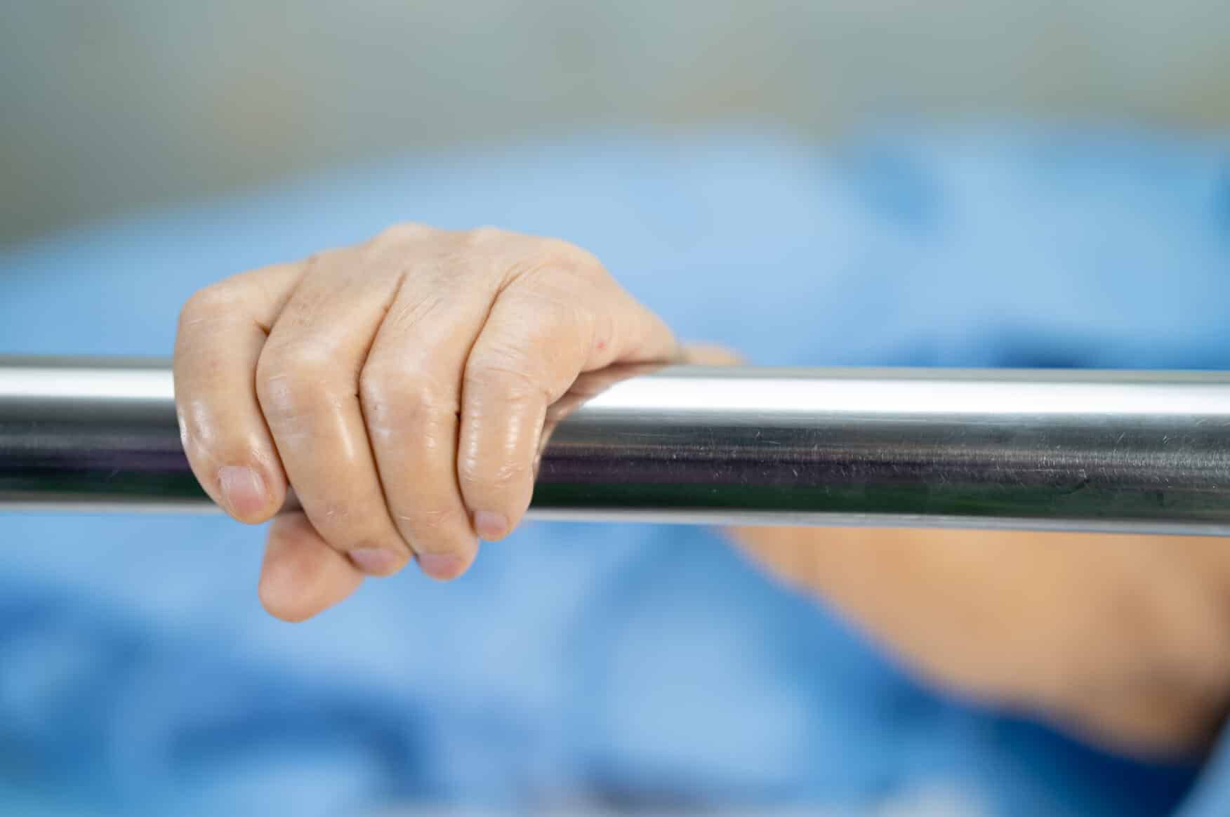 Elderly patient holding a bed rail, illustrating safe bed rail compliance in a UK care home