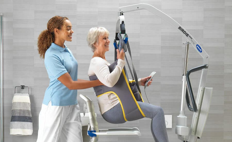 Carer assisting an older woman in a hoist using a patient lifting sling, shown as an example for a how to wash slings guide.