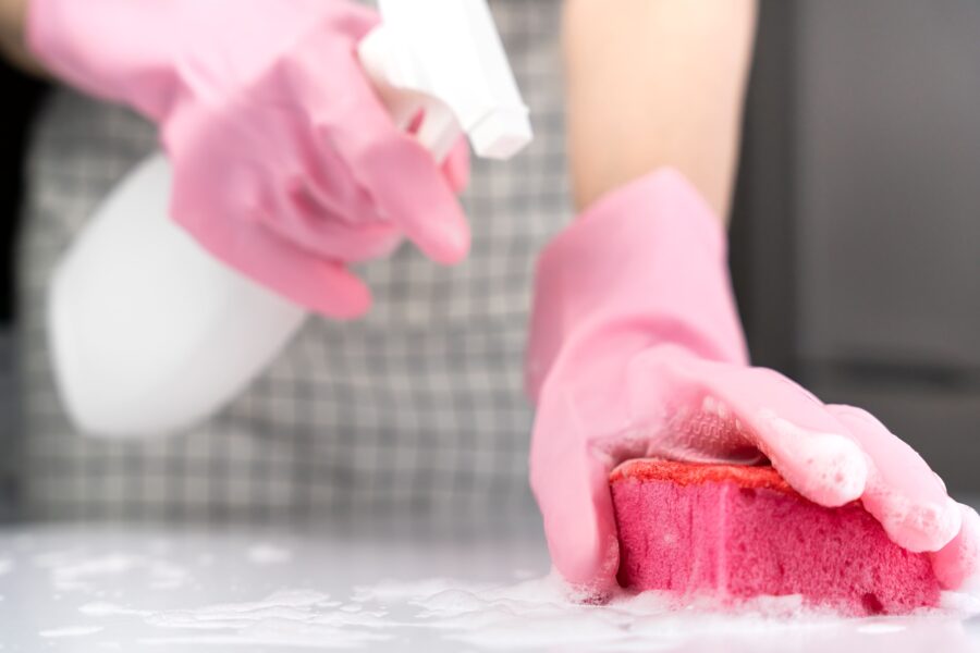 Person wearing pink gloves deep cleaning and disinfecting a surface with a sponge during a care home deep cleaning routine.